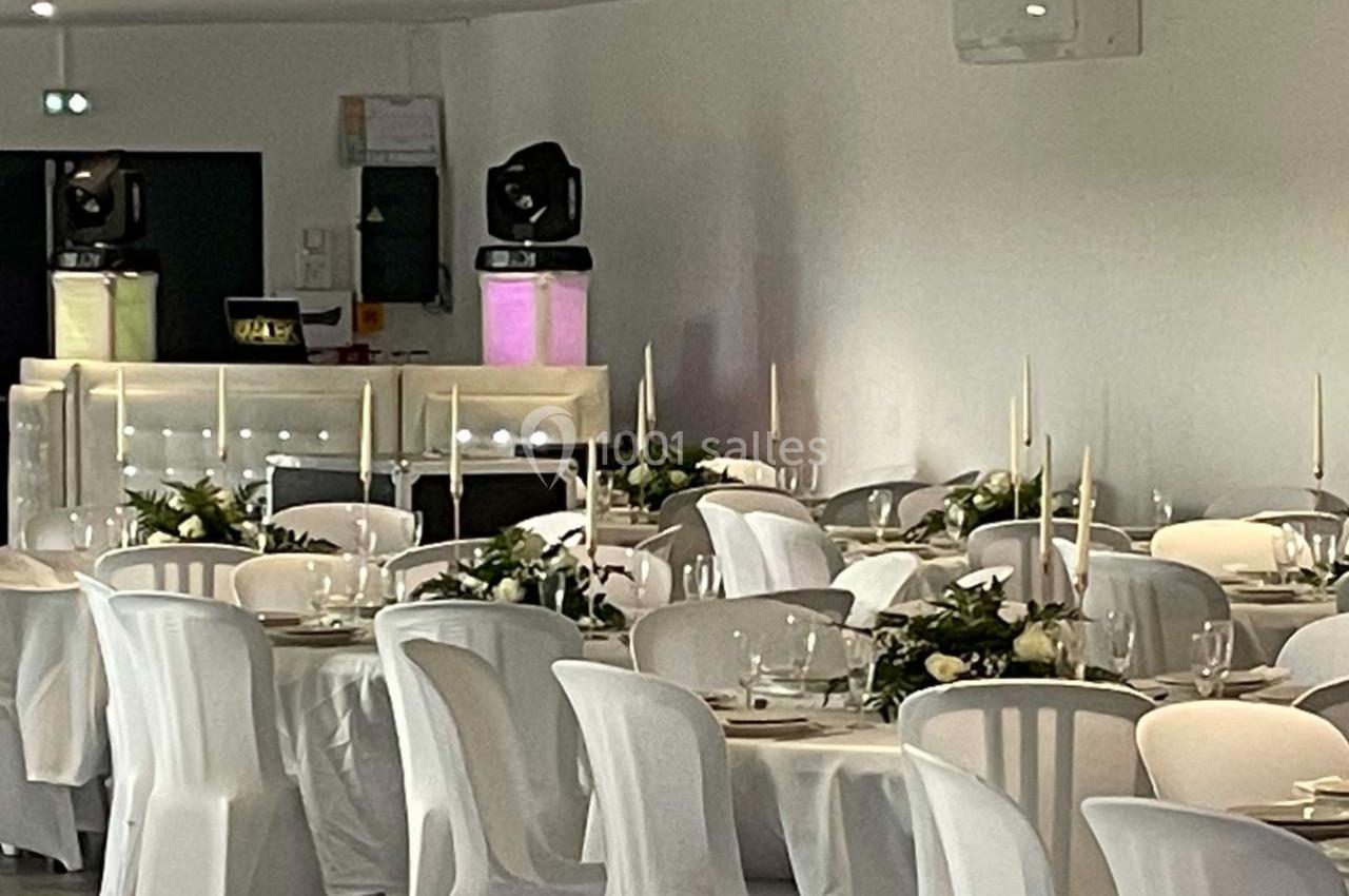 Salle de réception décorée avec des tables dressées, nappes blanches, chandeliers et compositions florales.