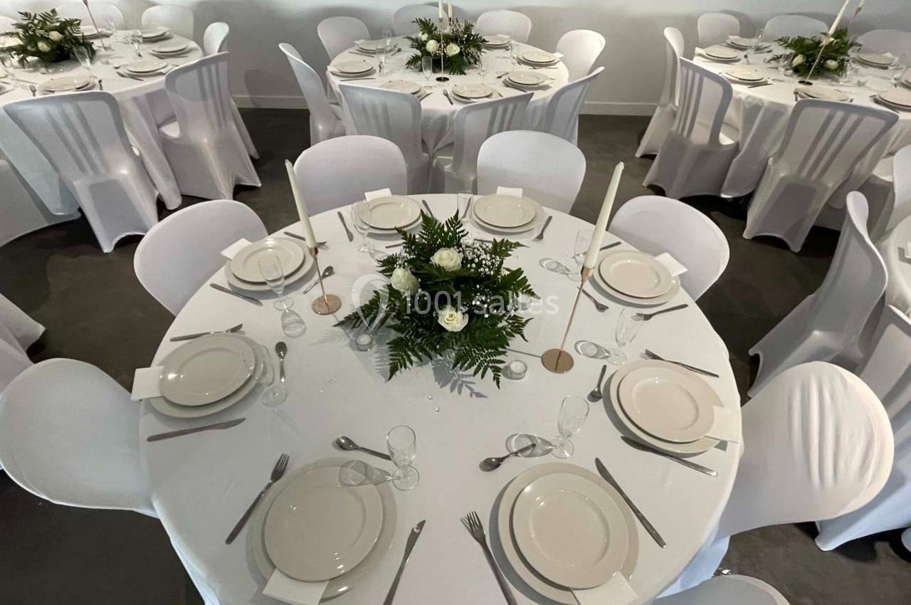 Tables rondes dressées avec nappes blanches, vaisselle élégante et centres de table composés de fleurs et de feuillage.