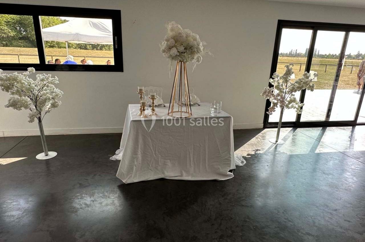 Table décorée avec une nappe blanche, des chandeliers dorés et un bouquet de fleurs, entourée de deux arbres artificiels.