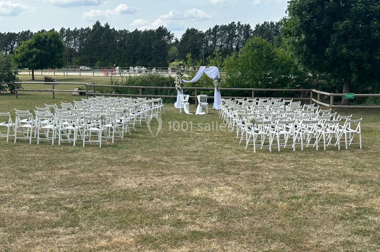 Chaises blanches disposées en extérieur autour d'une arche décorée pour une cérémonie sur une pelouse.