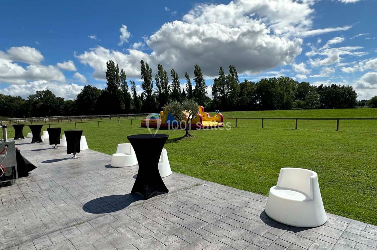 Espace extérieur avec pelouse, mobilier de réception et structure gonflable colorée sous un ciel partiellement nuageux.