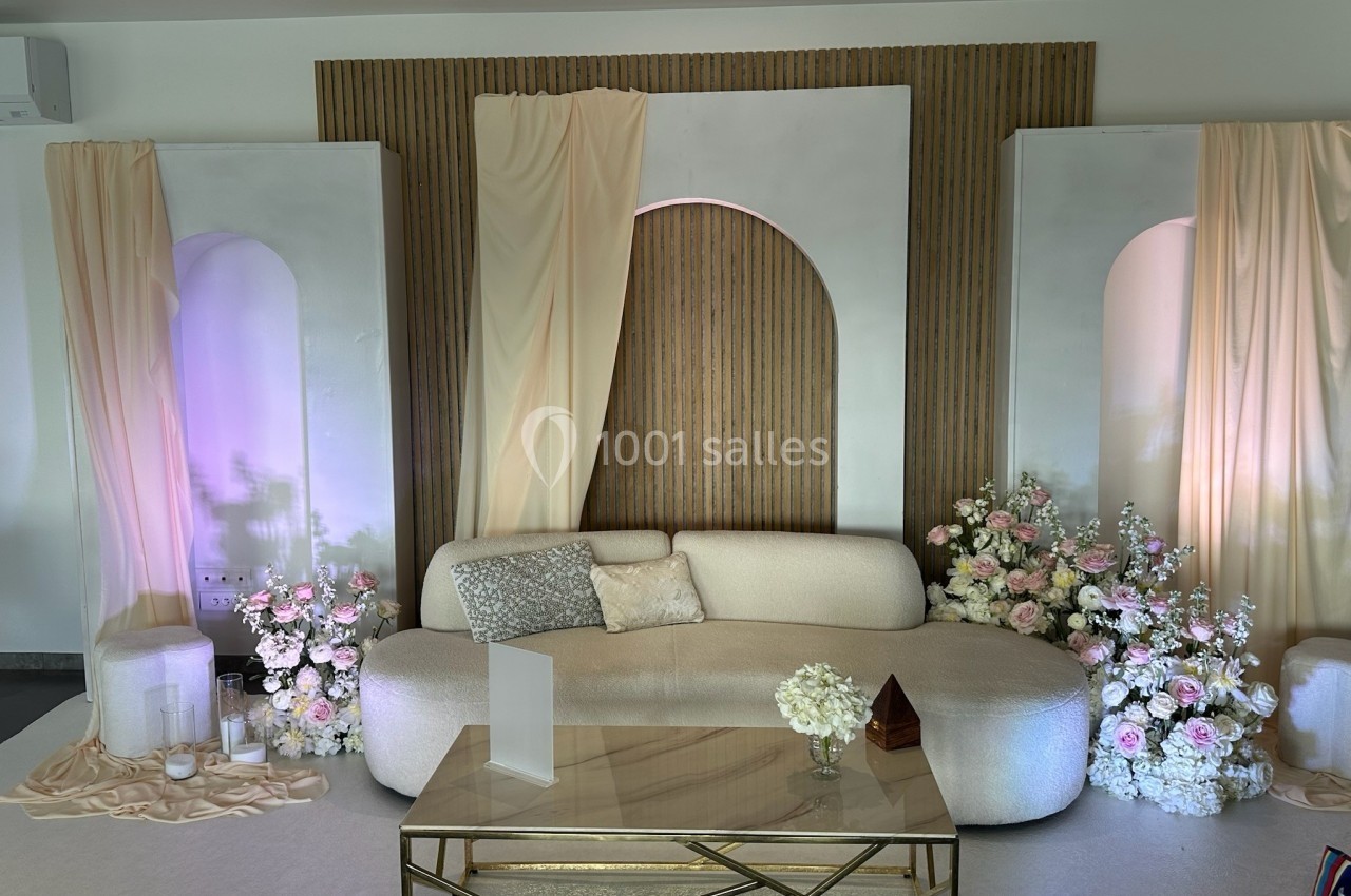 Décor intérieur élégant avec canapé beige, table basse dorée, fleurs blanches et roses, et rideaux crème.