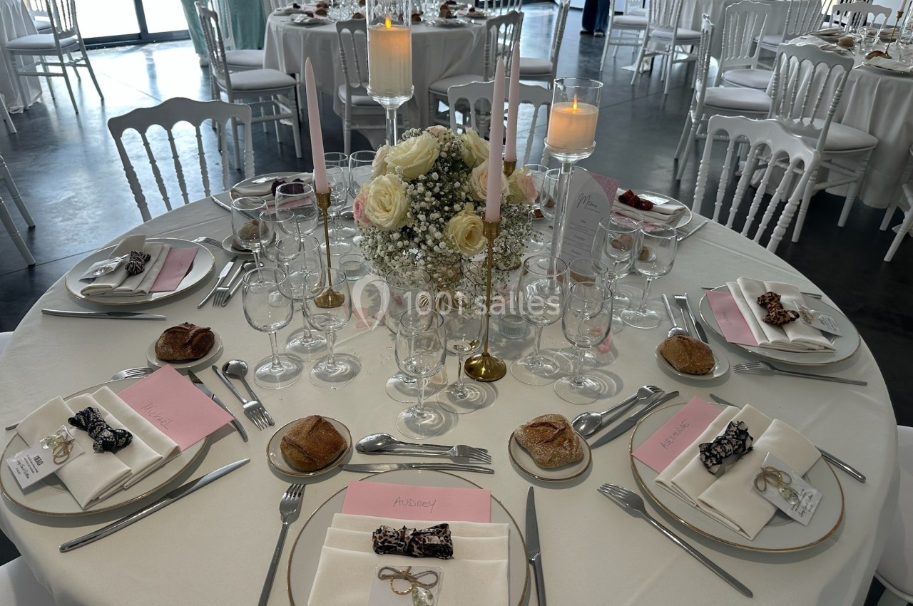 Table de réception élégamment dressée avec des fleurs, bougies, menus et couverts disposés autour d'assiettes.