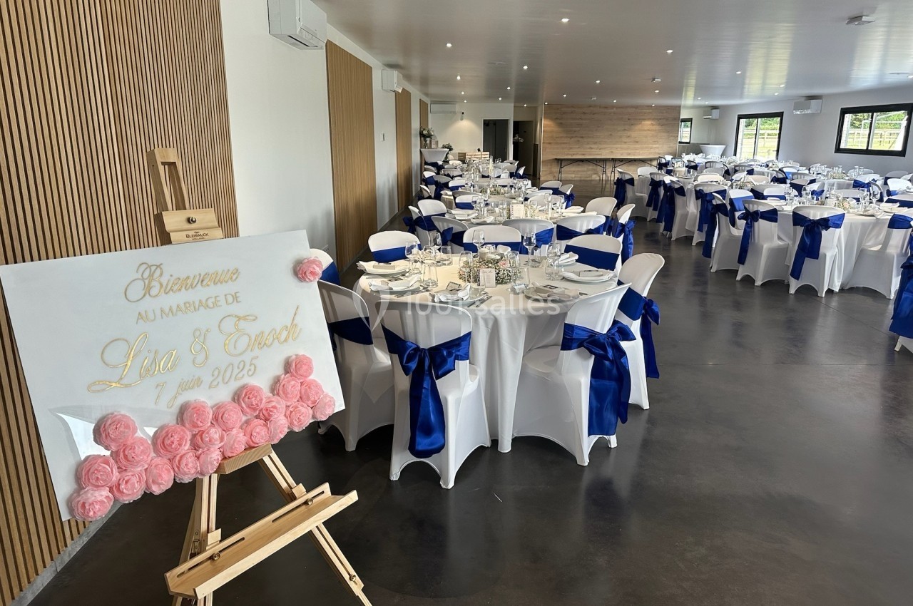 Salle de réception décorée pour un mariage avec des tables dressées et un chevalet affichant un message de bienvenue.