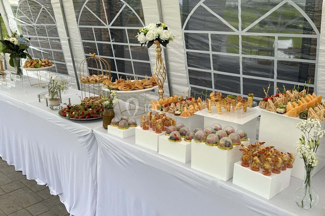 Buffet élégant avec verrines, fruits, pâtisseries et fleurs, disposé sur une table blanche sous une tente.