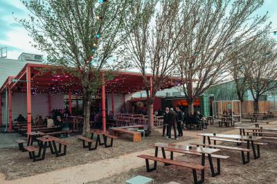 Salle lumineuse avec murs rouges, tables hautes en bois et métal, tabourets, affiches décoratives et luminaires modernes.