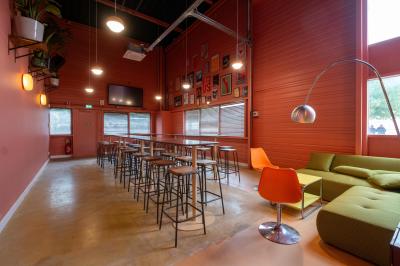 Salle lumineuse avec murs rouges, tables hautes en bois et métal, tabourets, affiches décoratives et luminaires modernes.