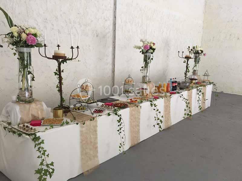 Table de buffet décorée avec des fleurs, chandeliers et guirlandes de lierre, proposant boissons et plats variés.