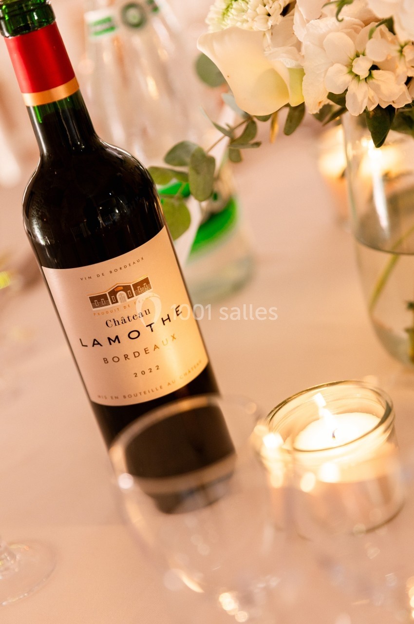 Bouteille de vin rouge Château Lamothe Bordeaux 2022 posée sur une table décorée de fleurs et de bougies.
