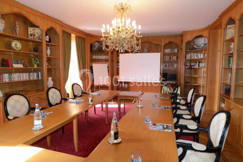 Salle de réunion avec tables en bois disposées en U, chaises élégantes, projecteur, tableau blanc et bibliothèque en arrière…