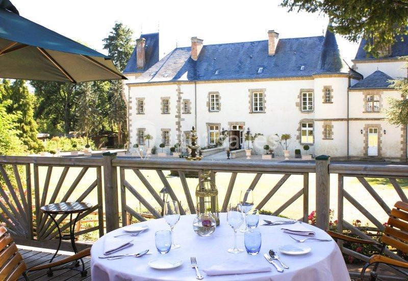 Table dressée sur une terrasse en bois avec vue sur un château entouré de verdure.