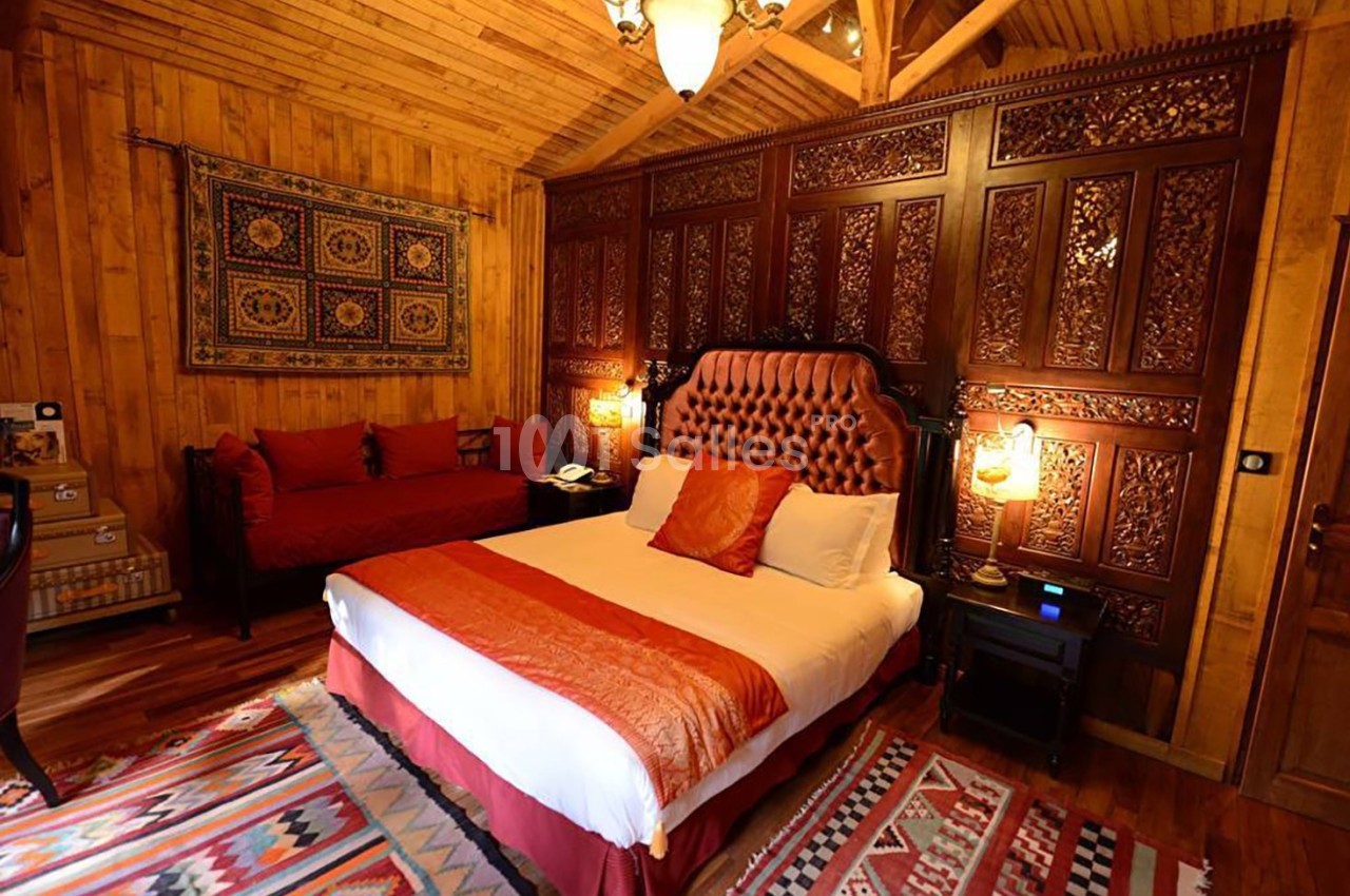 Chambre chaleureuse avec lit double, canapé rouge, murs en bois et panneaux sculptés, éclairée par des lampes douces.