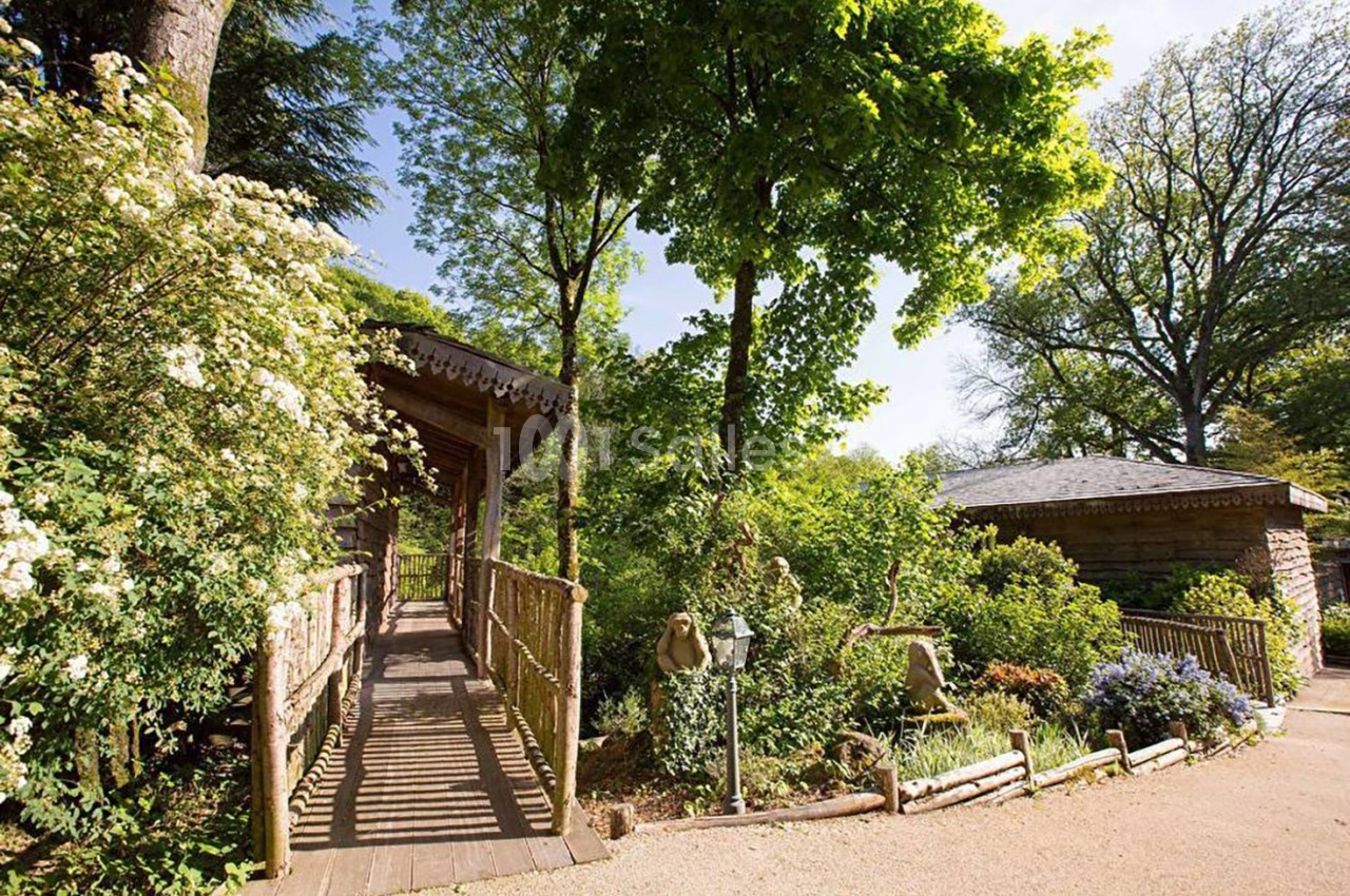 Passerelle en bois entourée de végétation luxuriante et reliant deux bâtiments dans un cadre naturel.