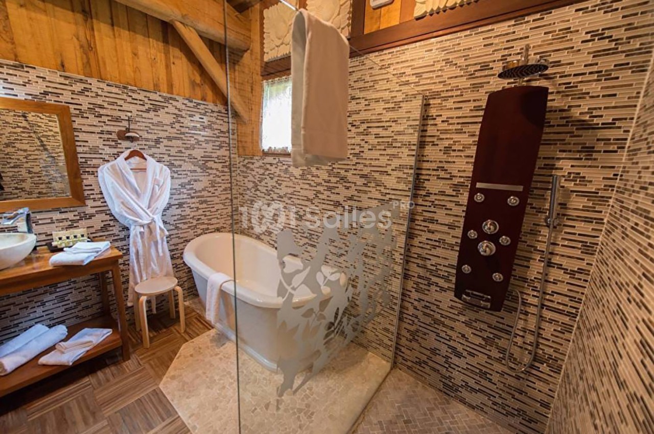Salle de bain avec baignoire, douche à l'italienne, peignoirs suspendus et murs en mosaïque beige et marron.