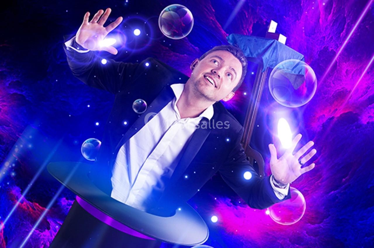 Un homme en costume semble émerger d'un chapeau magique, entouré de bulles et d'effets lumineux violets.