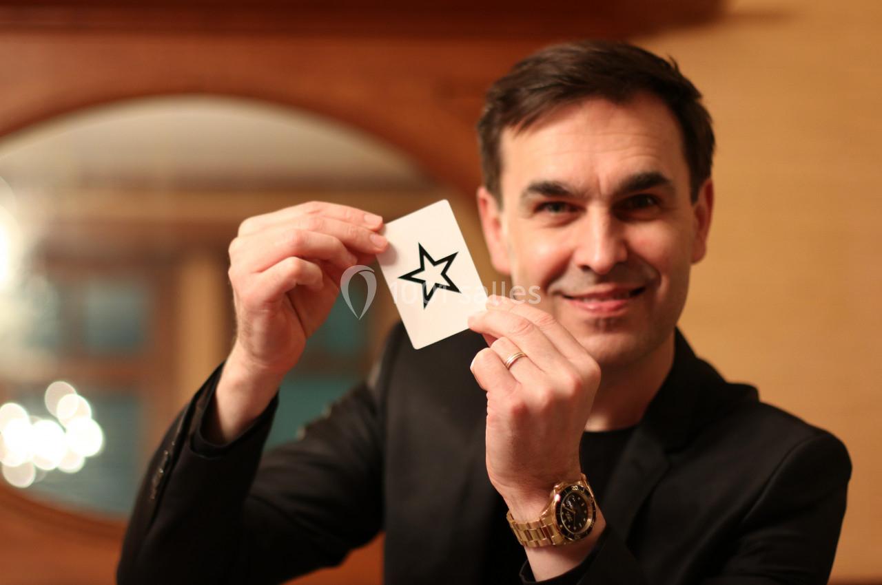 Un homme souriant tient une carte blanche avec une étoile noire imprimée, dans un intérieur chaleureux.