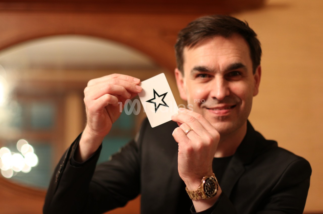 Un homme souriant tient une carte blanche avec une étoile noire imprimée, dans un intérieur chaleureux.