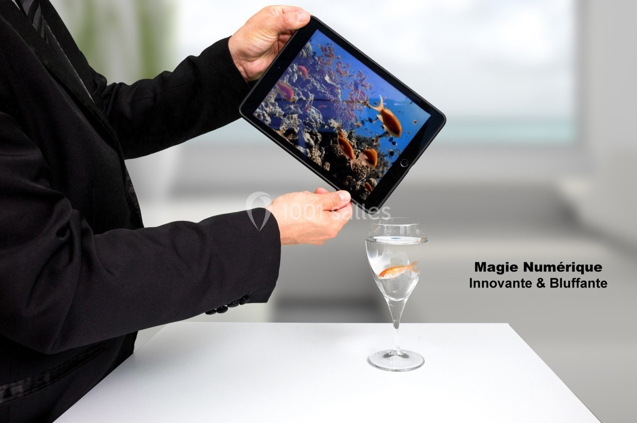 Un homme tient une tablette affichant un aquarium, alignée avec un verre contenant un poisson rouge.