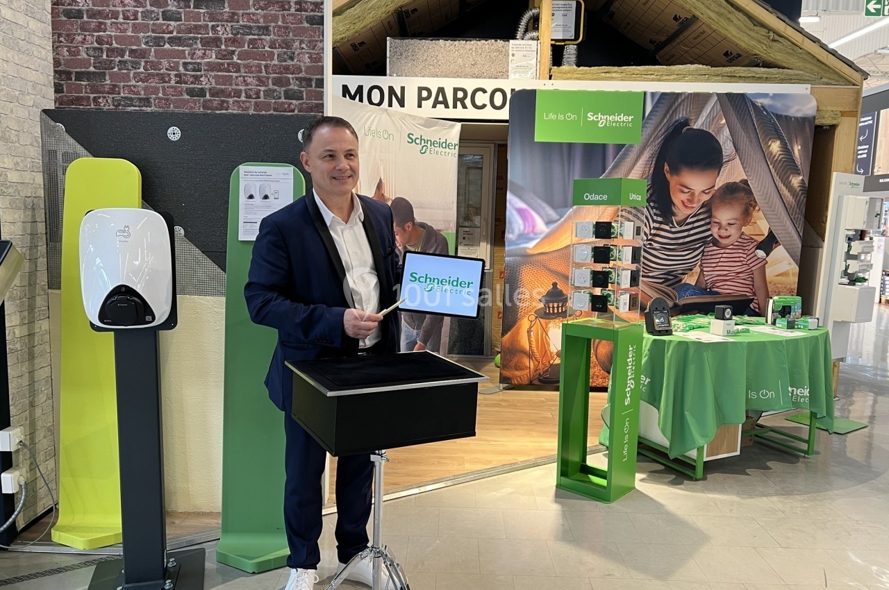Un homme présente un stand promotionnel avec des produits Schneider Electric dans un espace d'exposition.