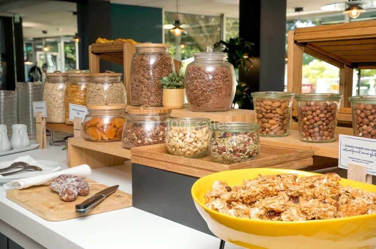 Location salle Orgeval (Yvelines) - Novotel Poissy Orgeval #11 Buffet de petit-déjeuner avec céréales, fruits secs, noix et granola présentés dans des bocaux en verre et un saladier.