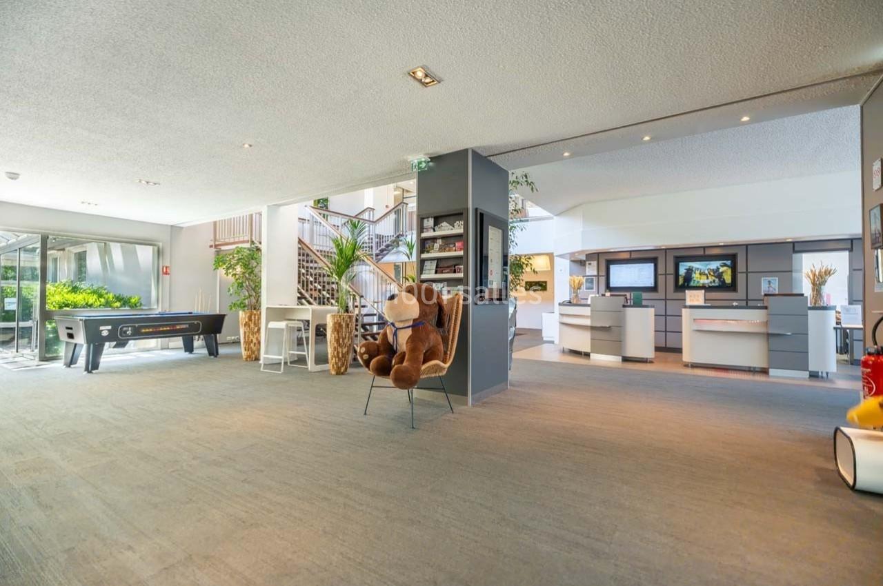 Location salle Orgeval (Yvelines) - Novotel Poissy Orgeval #7 Hall d'accueil spacieux avec fauteuil, peluche, baby-foot, escalier et comptoirs d'information en arrière-plan.