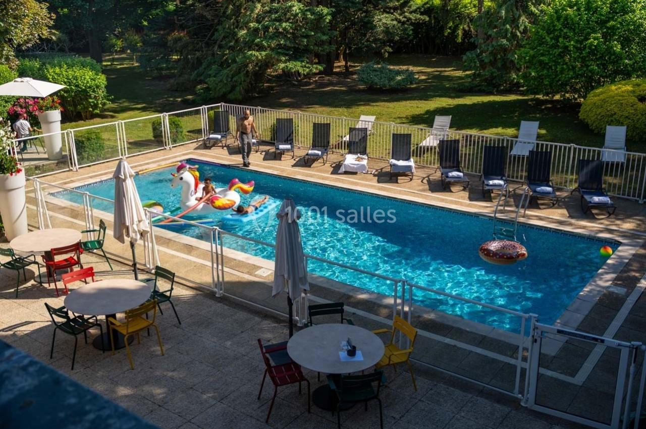 Location salle Orgeval (Yvelines) - Novotel Poissy Orgeval #19 Piscine extérieure entourée de chaises longues, tables et chaises colorées, avec des jouets gonflables dans l'eau.
