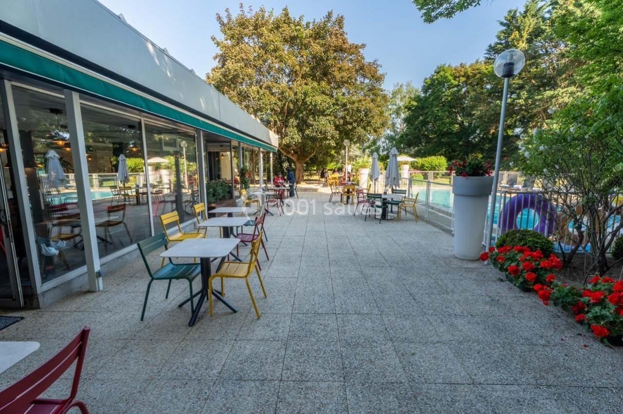 Location salle Orgeval (Yvelines) - Novotel Poissy Orgeval #25 Terrasse extérieure avec tables et chaises colorées, bordée de fleurs et donnant sur une piscine entourée d'arbres.