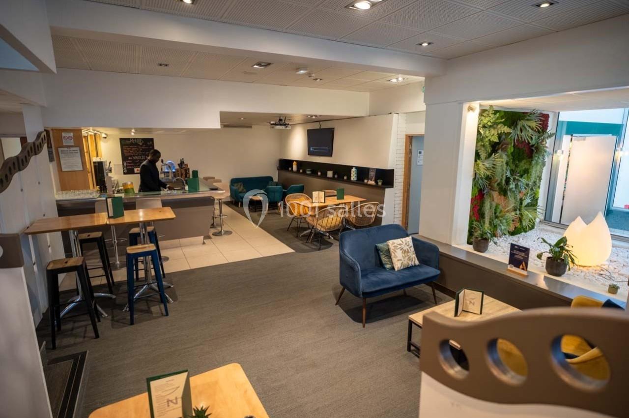 Location salle Orgeval (Yvelines) - Novotel Poissy Orgeval #29 Espace lounge lumineux avec tables, chaises, fauteuils et mur végétal, aménagé pour détente ou travail.