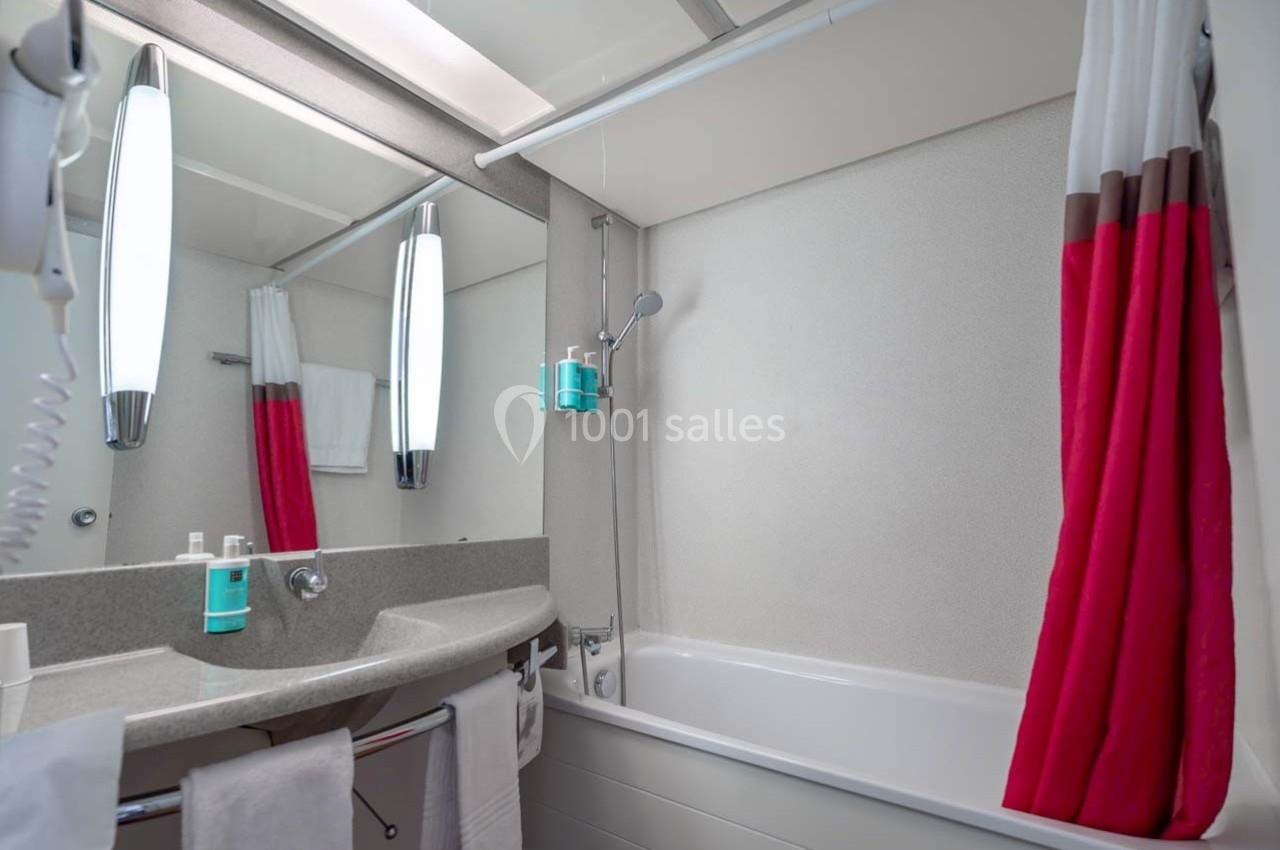 Location salle Orgeval (Yvelines) - Novotel Poissy Orgeval #35 Salle de bain avec lavabo, miroir, baignoire, douchette murale et rideau rouge et blanc.