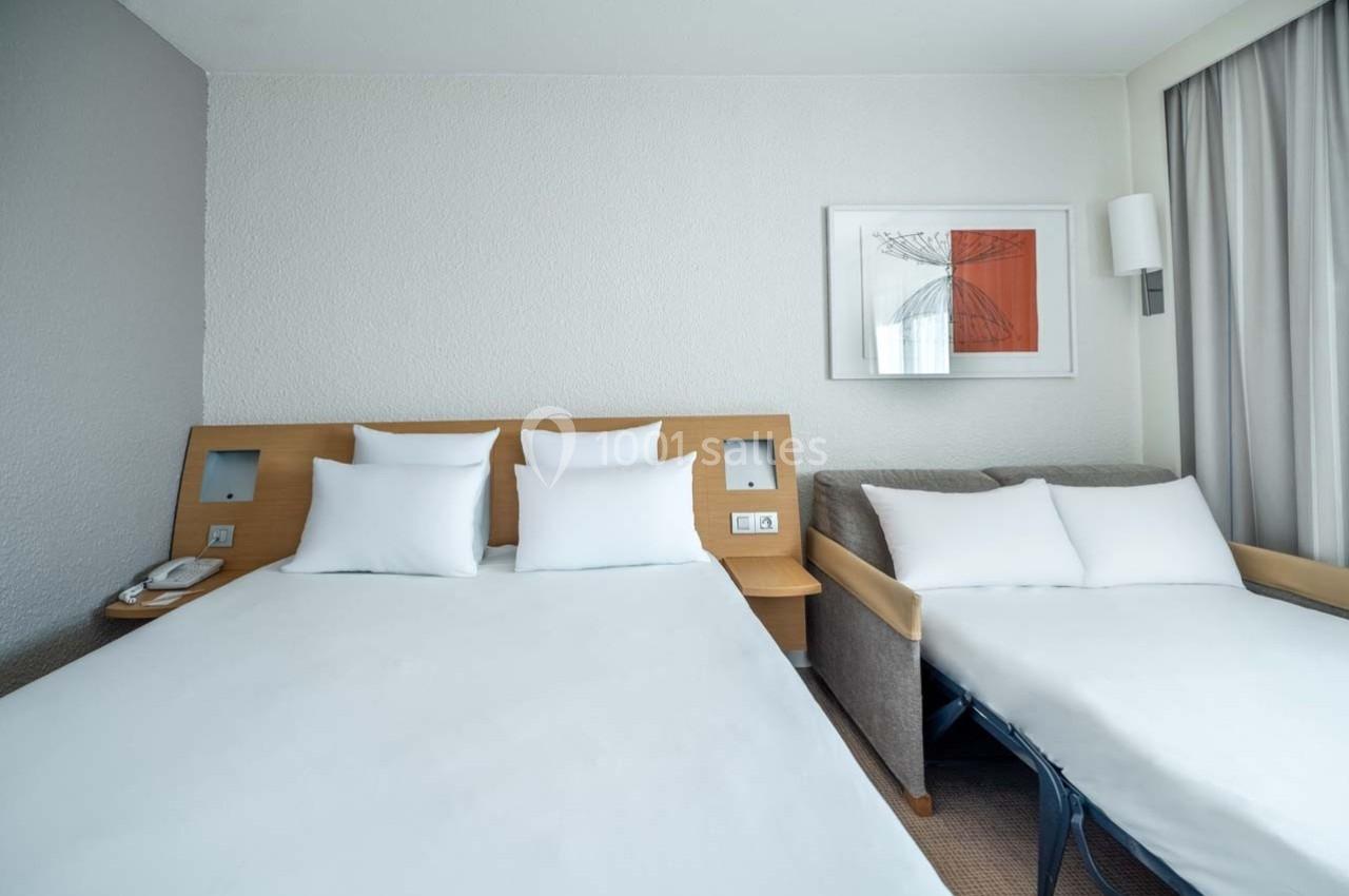 Location salle Orgeval (Yvelines) - Novotel Poissy Orgeval #38 Chambre d'hôtel avec un lit double, un canapé-lit, des draps blancs et un tableau encadré sur le mur.
