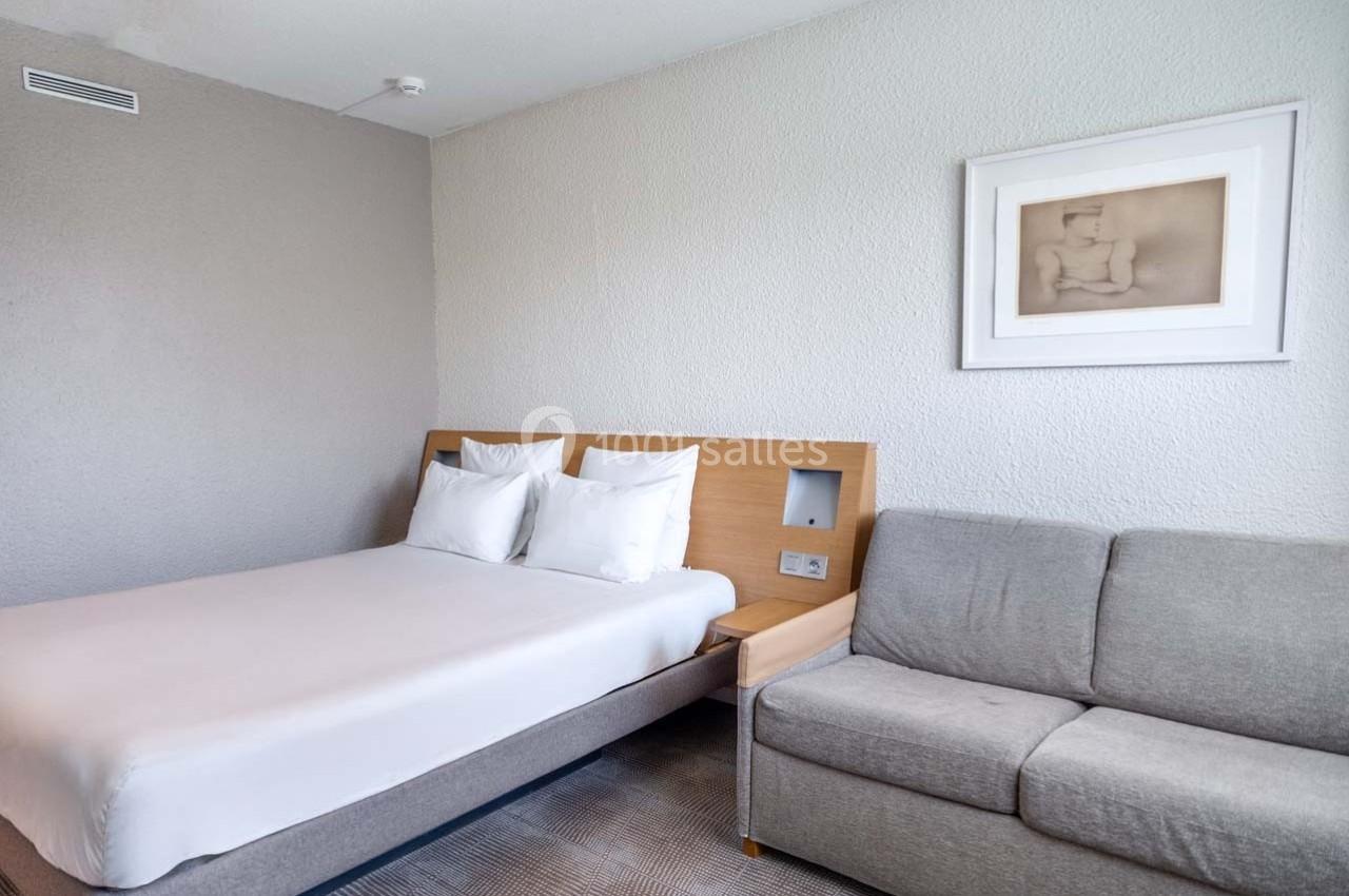 Location salle Orgeval (Yvelines) - Novotel Poissy Orgeval #43 Chambre d'hôtel avec un lit double, un canapé gris, un mur blanc et un tableau encadré.
