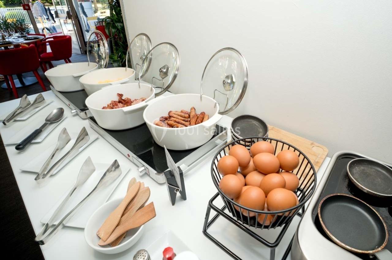Location salle Orgeval (Yvelines) - Novotel Poissy Orgeval #44 Buffet de petit-déjeuner avec œufs, saucisses, bacon et ustensiles disposés sur un comptoir blanc.