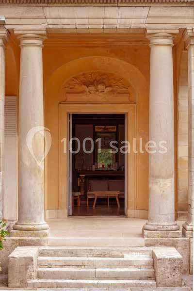 Entrée d'un bâtiment avec des colonnes en pierre, une porte ouverte et un intérieur visible en arrière-plan.
