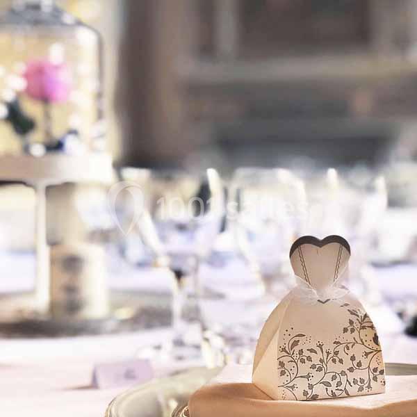 Boîte cadeau en forme de robe blanche avec motifs dorés, posée sur une table décorée pour un événement festif.