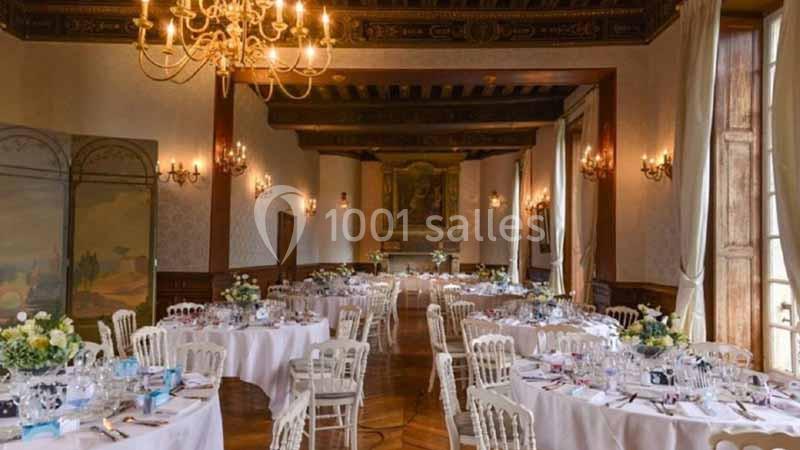 Salle de réception élégante avec tables rondes dressées, décorations florales et éclairage chaleureux.