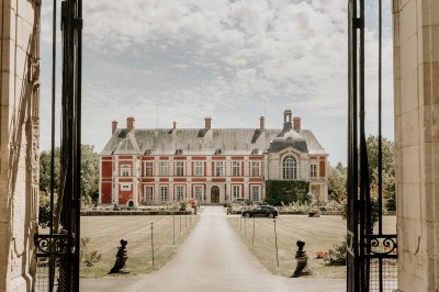 Miniature Location salle Lésigny (Seine-et-Marne) - Château de Lésigny #5 Façade d'un bâtiment ancien avec porte en bois sculpté, grandes fenêtres et allée bordée de fleurs rouges.