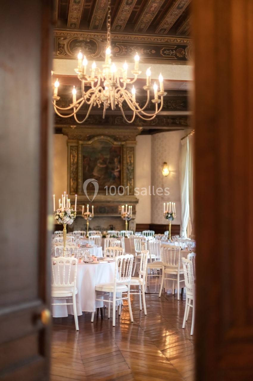 Salle de réception élégante avec tables dressées, chaises blanches et lustre suspendu sous un plafond décoré.