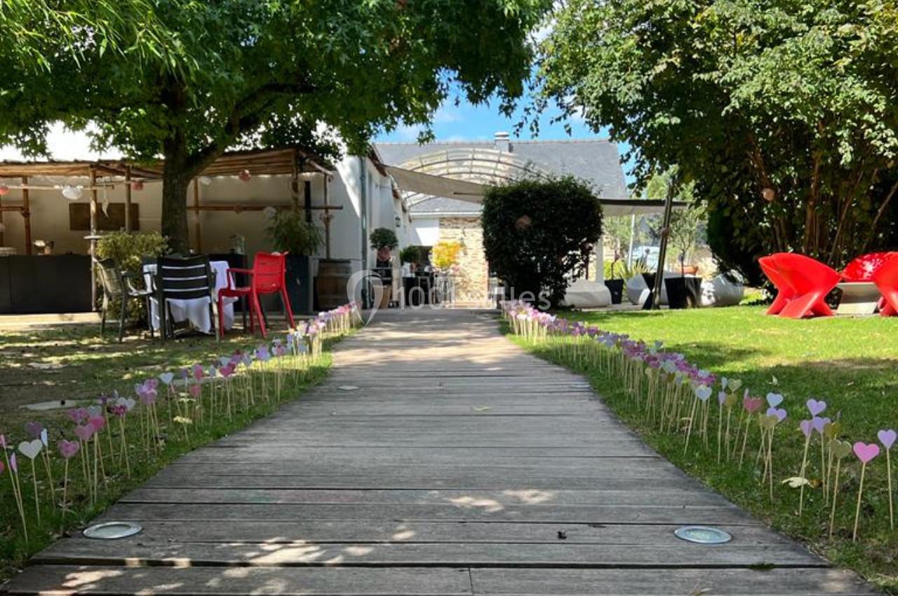 Allée en bois bordée de petits cœurs colorés plantés dans l'herbe, menant à une terrasse ombragée.