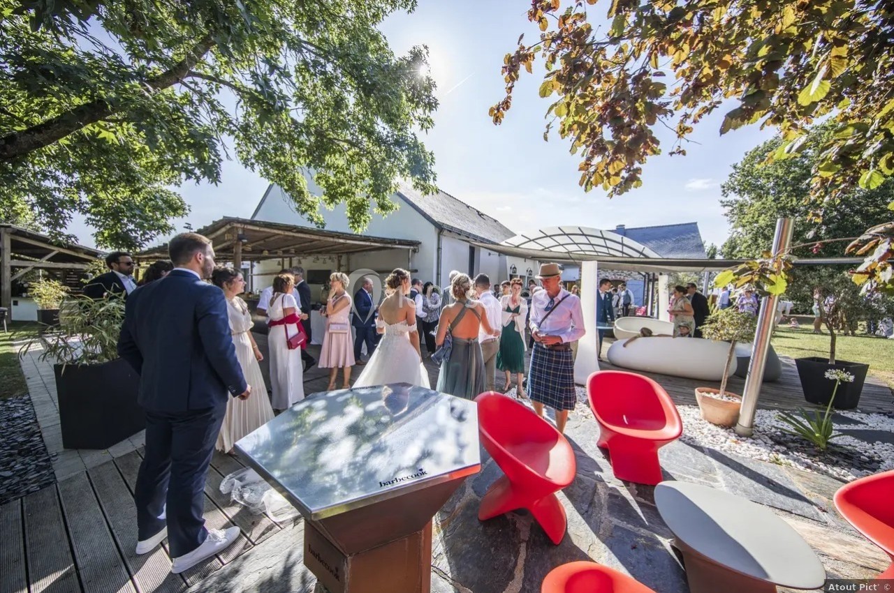 Groupe de personnes rassemblées en extérieur près de bâtiments blancs, entourés d'arbres et de mobilier moderne.