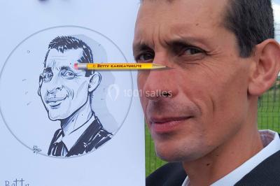 Un homme souriant tient un dessin caricatural de lui-même, réalisé avec des détails humoristiques.