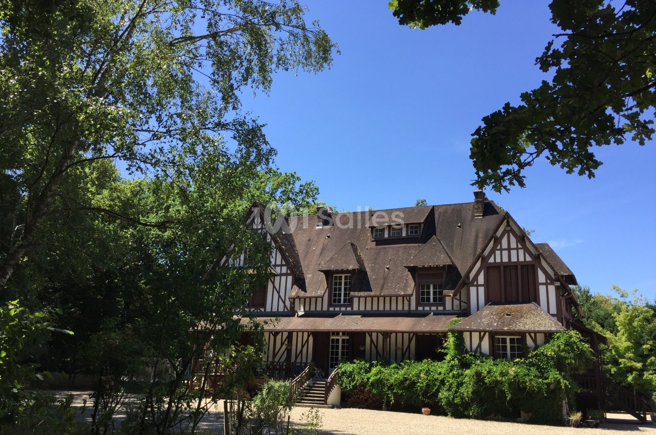 Maison à colombages entourée de végétation, avec un ciel bleu dégagé en arrière-plan.