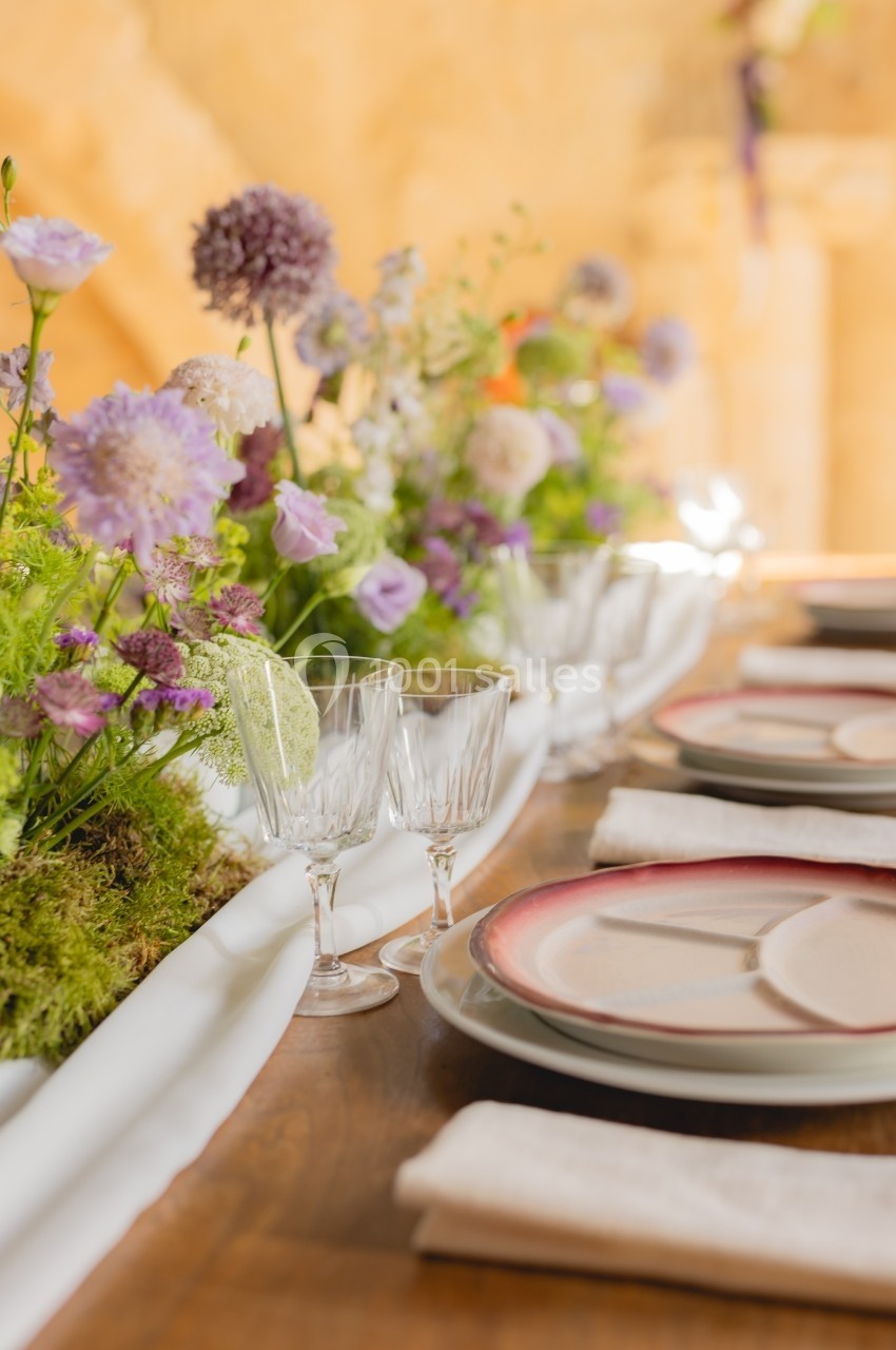 Table décorée avec des fleurs pastel, verres en cristal, assiettes élégantes et serviettes blanches.