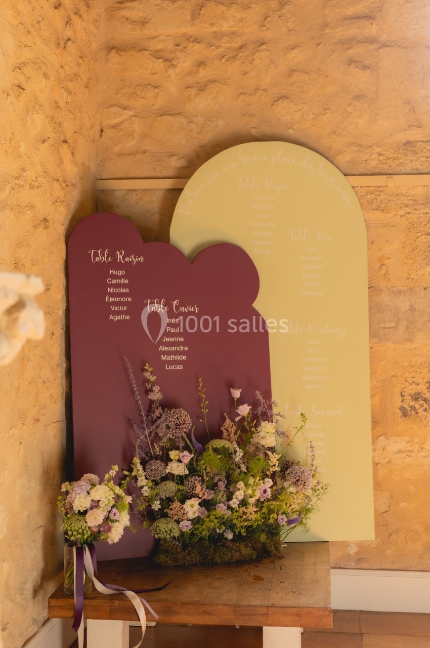 Deux panneaux de plan de table de mariage, l'un violet et l'autre jaune, décorés de fleurs dans un coin en pierre.