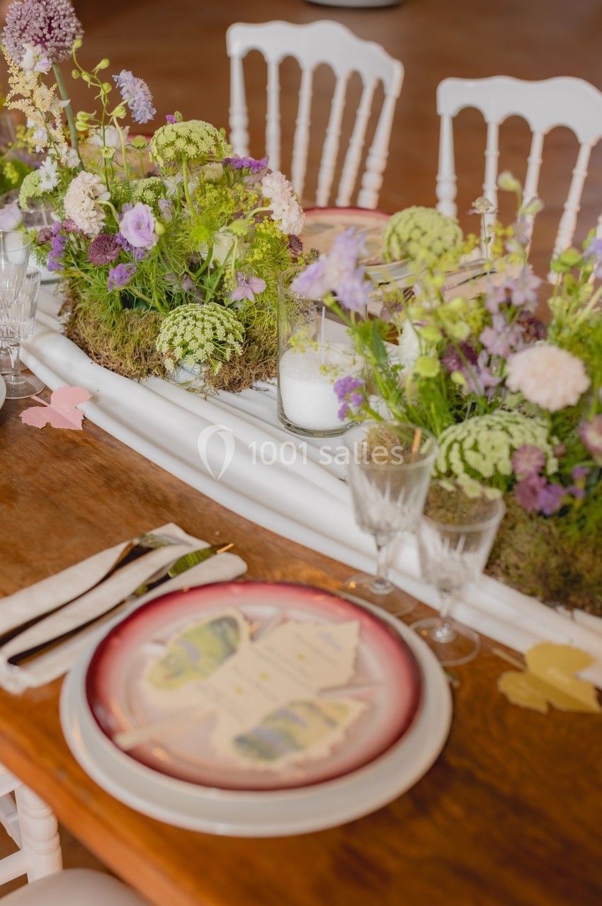Table décorée avec des fleurs champêtres, vaisselle élégante et menus posés sur des assiettes.