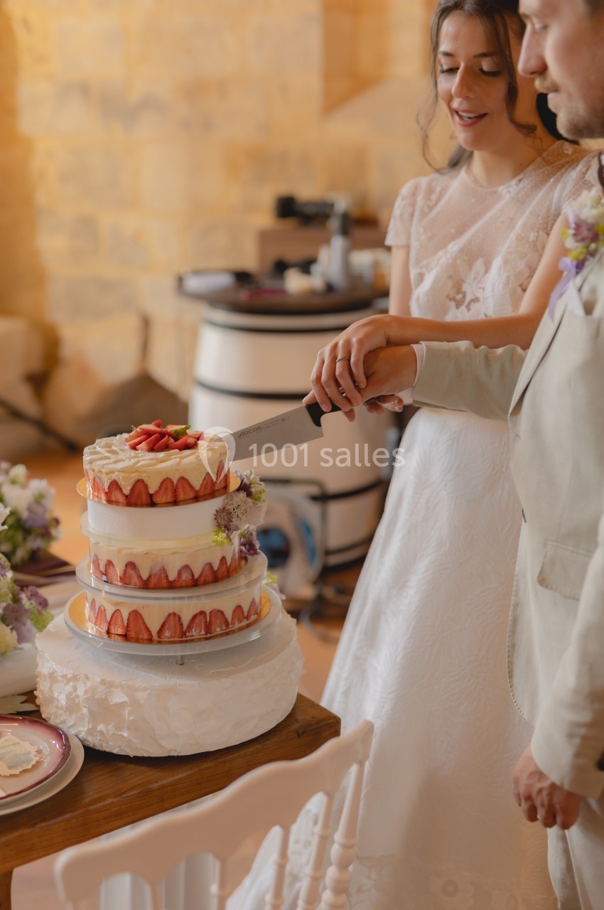 Un couple en tenue de mariage coupe ensemble un gâteau à étages décoré de fraises et de fleurs.
