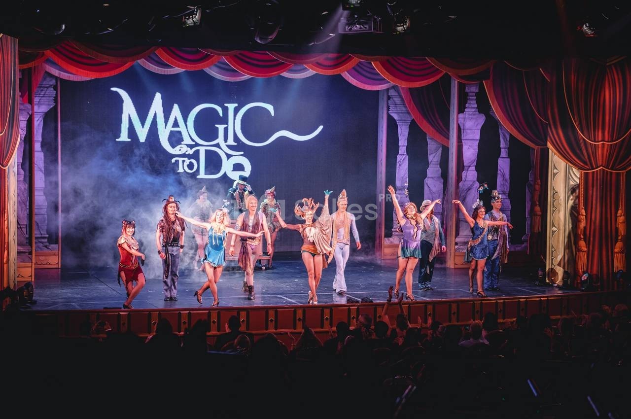 Spectacle sur scène avec des artistes costumés dansant devant un décor lumineux et un rideau rouge.