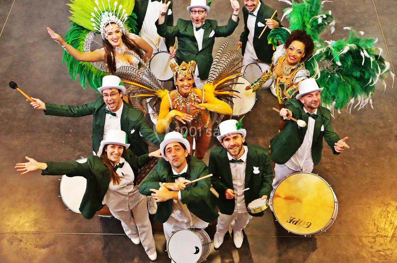 Groupe de musiciens en costumes verts et blancs accompagnés de danseuses en tenues colorées et plumes, vu de dessus.