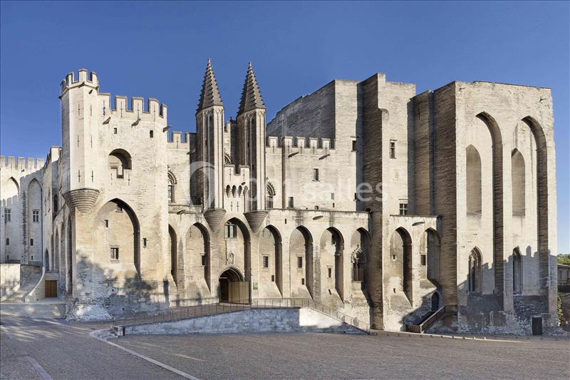 Façade du Palais des Papes à Avignon, imposant bâtiment médiéval en pierre avec tours et arcs gothiques.