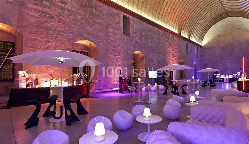 Salle voûtée éclairée avec des lumières colorées, aménagée avec des tables, fauteuils modernes et parasols lumineux.