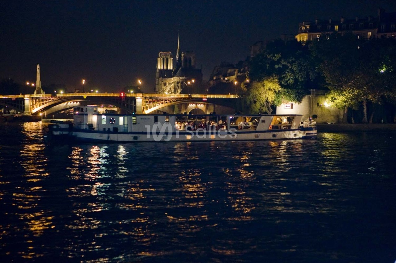 Bateau naviguant sur la Seine de nuit, avec Notre-Dame et un pont illuminé en arrière-plan.